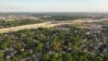 An aerial view of expressway crisscrossing South Milwaukee with neighborhoods flanking the express way. There are abundant green trees and a clear blue sky above.