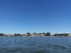 A photo taken from Pewaukee Lake in Pewaukee, Wisconsin, with beachgoers in the background on the shore below a clear blue sky.