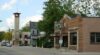 A view of one side of the main street that goes through downtown Thiensville, Wisconsin, with a row of one-story buildings and a two-story building with a bell tower in the background.