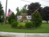 A sign that reads "Welcome to Belgium" is flanked by trees and two American flags.