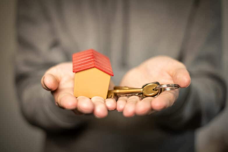 A close-up photo of a pair of hands holding a tiny house in one hand and a key in the other.