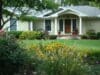 Shrubs are in the foreground with a green lawn and a well-kept house in the background.