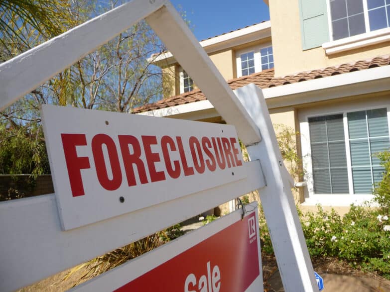 A sign that reads "Foreclosure" written in red in front of a house.