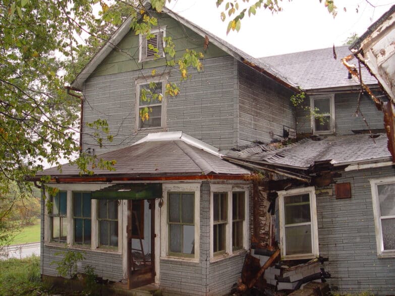 A frontal view of a dilapidated two-story house with part of its roof caving in due to water damage