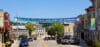 Under a clear blue sky is the main thoroughfare in Downtown Janesville with a banner hanging over the street that reads, “Open doors. Open hearts. Enjoy Downtown Janesville