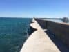 Under a clear blue sky a breakwater concrete pier extends into Lake Michigan on the shores of Port Washington, Wisconsin. On the left side is rough water. On the right side the water is placid and there’s a yacht
