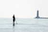 The silhouette of a man standing on a paddle board on Lake Michigan with the Sheboygan lighthouse in the distance.