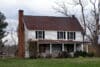 A somewhat ramshackle, slightly dilapidated two-story house with a dullish-red roof and white siding.