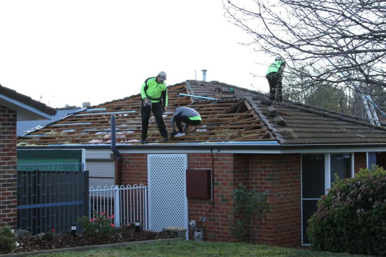 Roofers stand on a roof of a house as they make repairs.